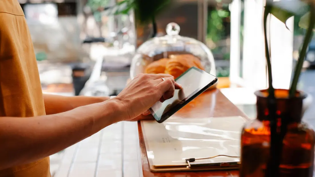 Mani che gestiscono gli ordini su un tablet al bancone di un locale